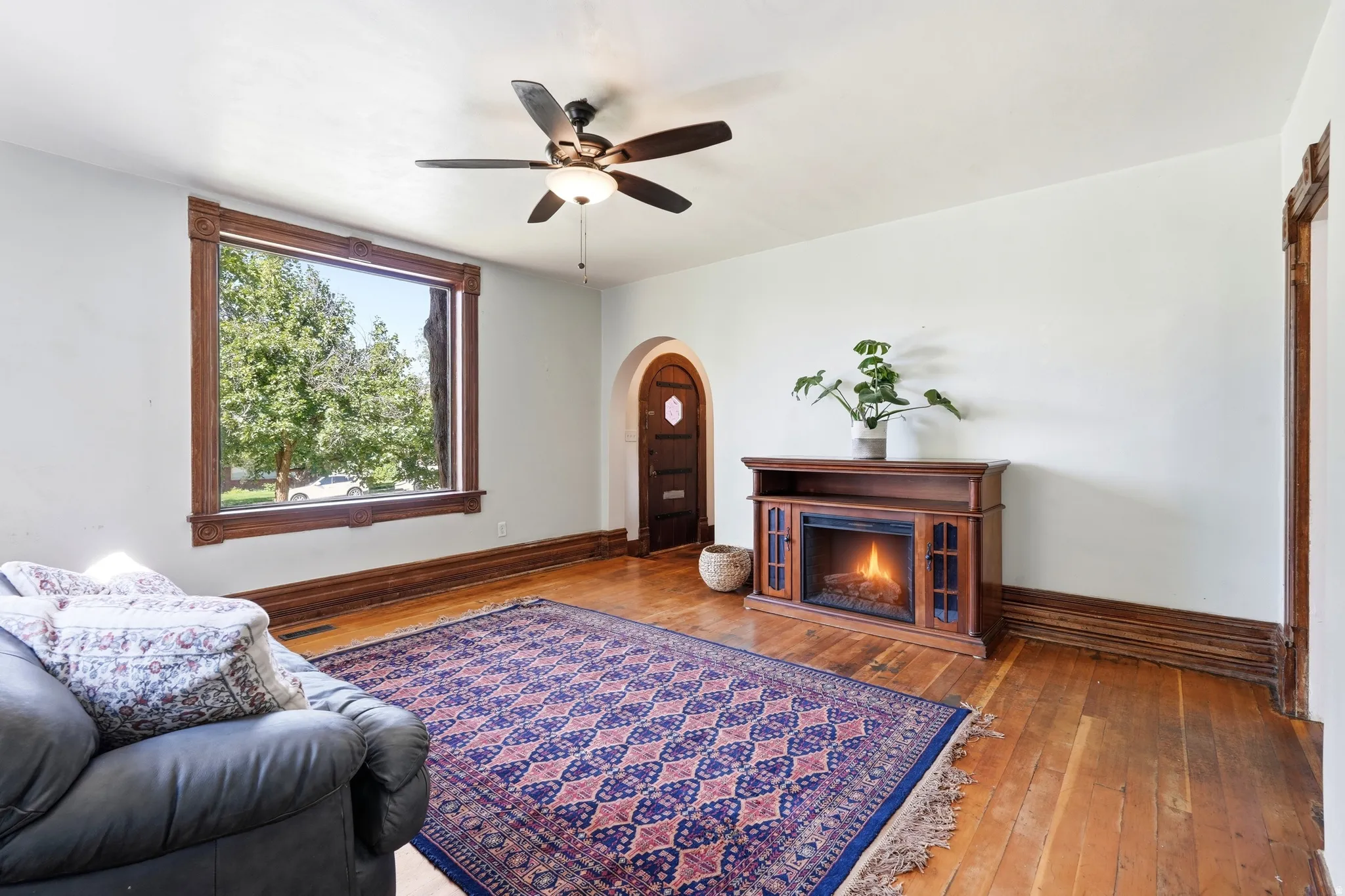 Living space featuring wood-finish flooring, a decorative wood-framed window, and a ceiling fan