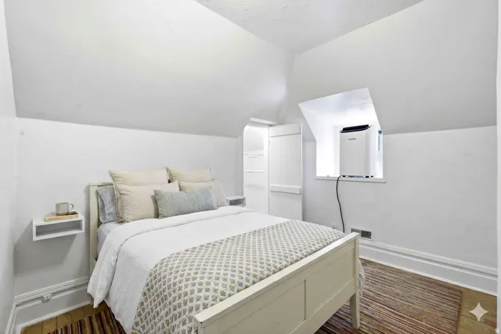 Attic bedroom featuring an angled ceiling, wood-finish flooring, a built-in window nook, and white painted trim