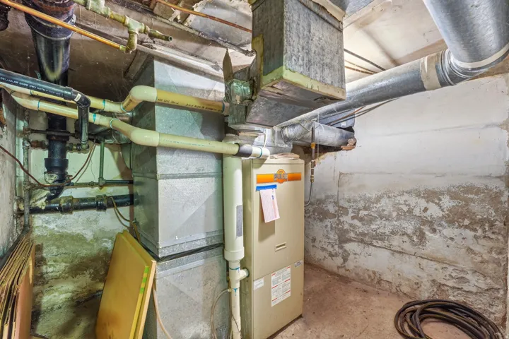 Utility area featuring a central forced-air furnace, interconnected ductwork, and exposed plumbing lines