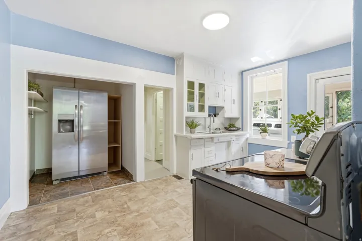 Kitchen featuring white cabinetry, a stainless steel side-by-side refrigerator, a white sink, light-toned flooring, and a large window with white trim