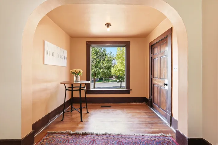 Archway entry featuring hardwood flooring, a multi-paneled wood door, dark wood trim, and a window with exterior views