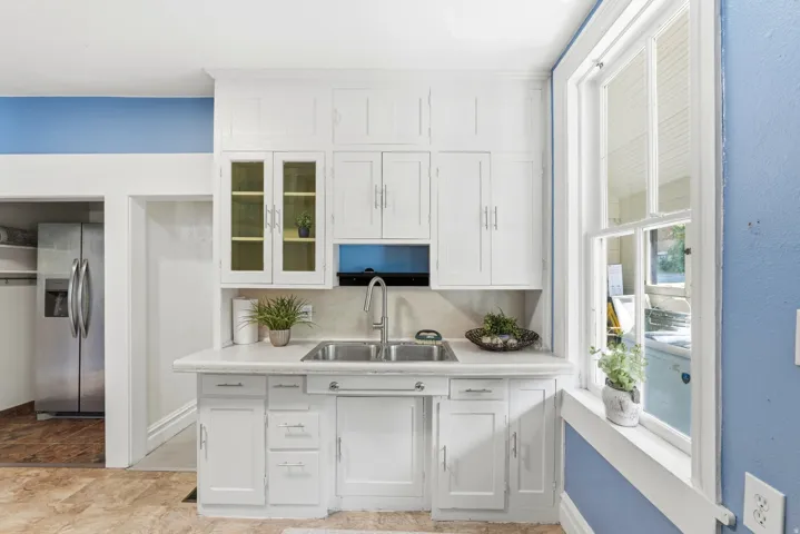 Kitchen area featuring white cabinetry, a double basin stainless steel sink with a gooseneck faucet, light-toned countertops, and a large multi-pane window