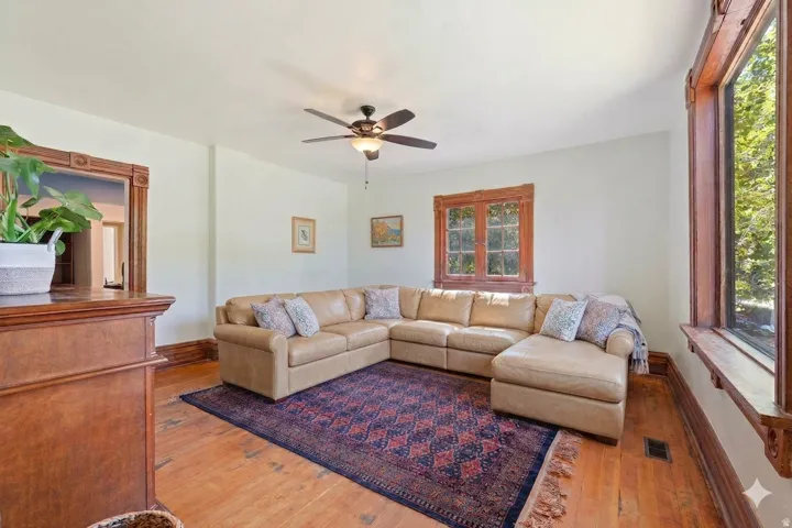 Living area featuring wood-finish flooring, white walls, and a ceiling fan