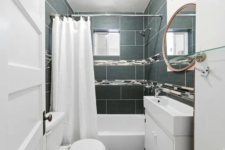 Bathroom featuring floor-to-ceiling dark gray tile, a decorative mosaic accent band, and a window above the tub