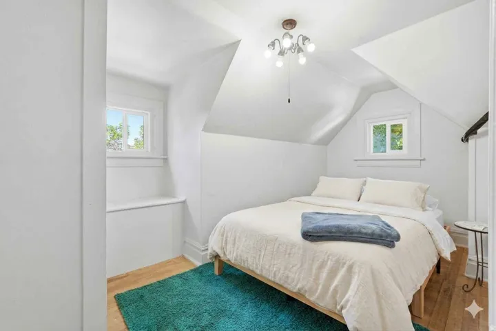 Attic room featuring sloped ceilings, two windows with white trim, and light wood-finish flooring