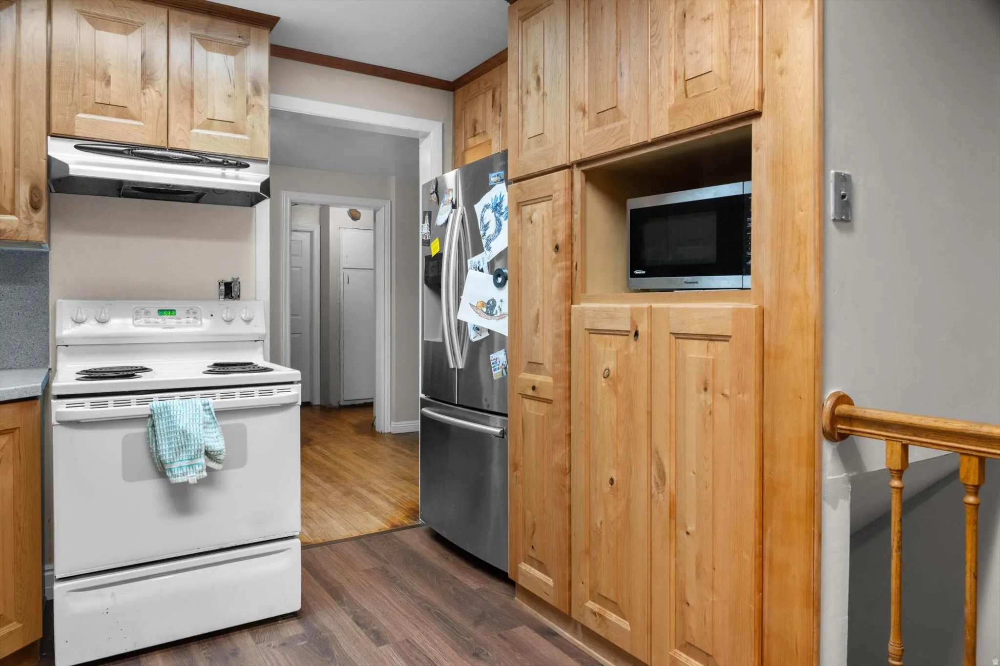 Kitchen featuring wood cabinetry, stainless steel refrigerator, white electric range with overhead vent, built-in microwave, and wood-finish flooring