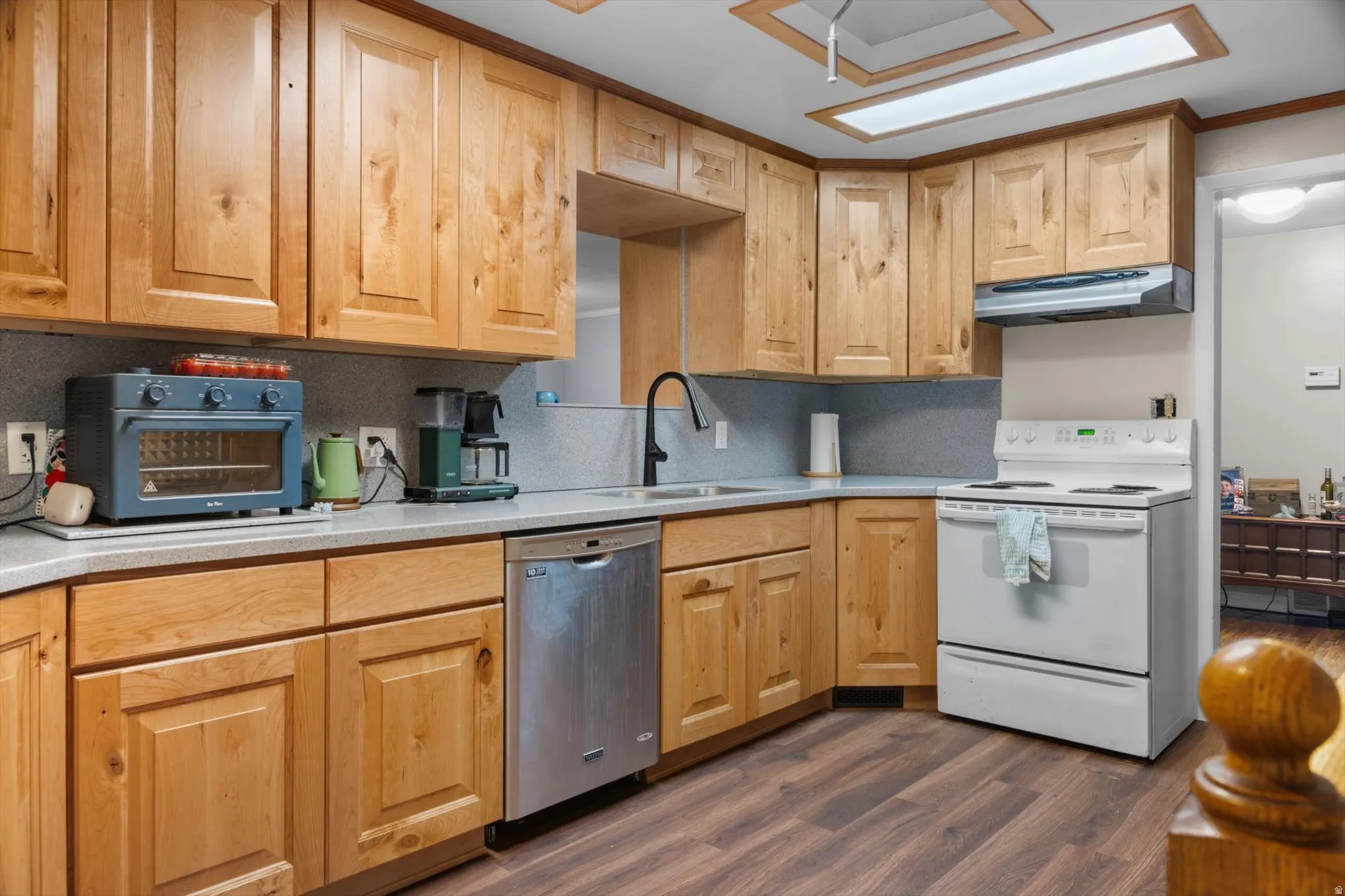 Kitchen featuring light wood cabinetry, light grey countertops, a stainless steel dishwasher, a white electric range with an overhead vent hood, and wood-finish flooring