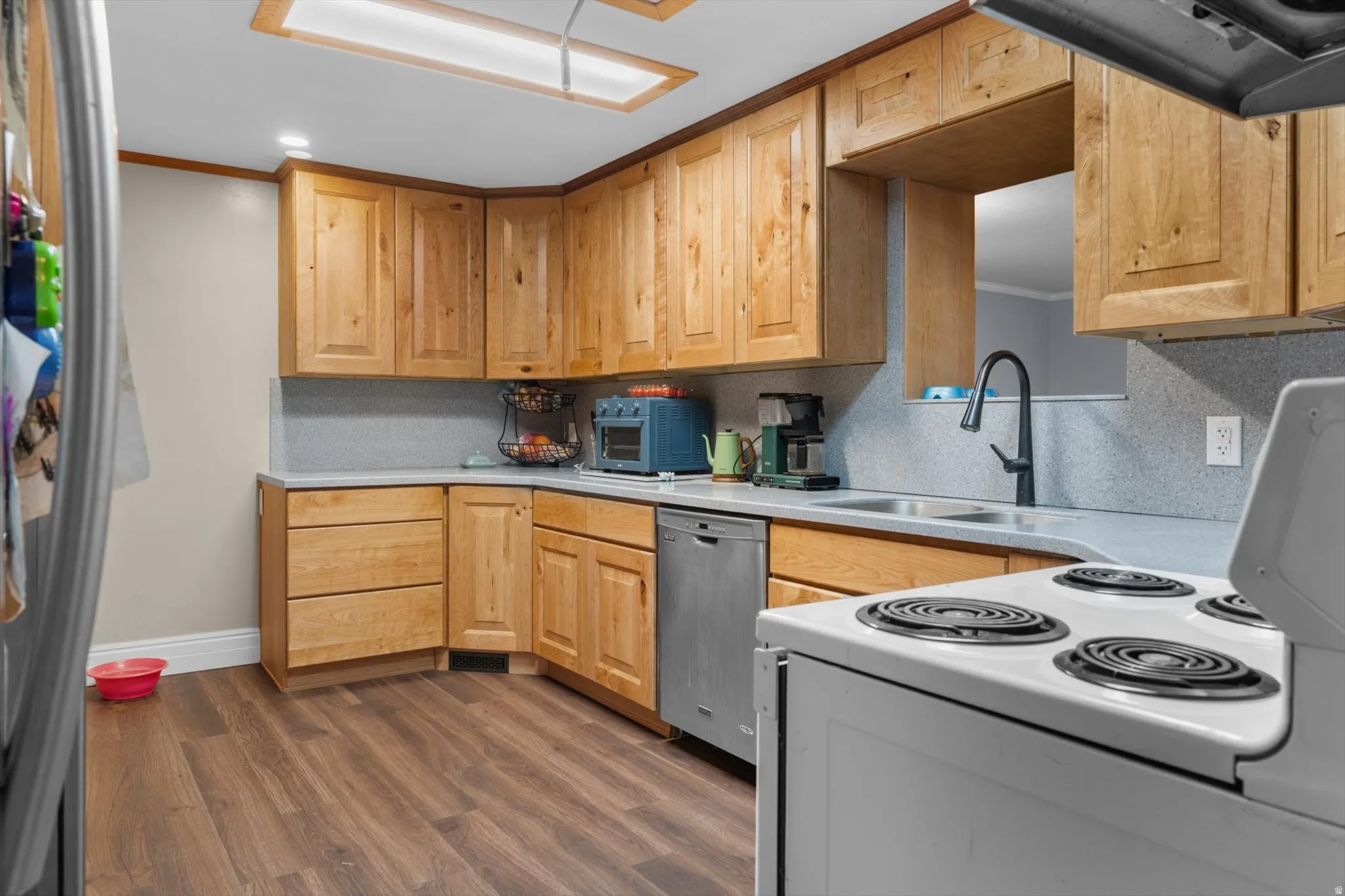 Kitchen featuring wood-finish cabinetry, light-toned countertops, and a stainless steel dishwasher