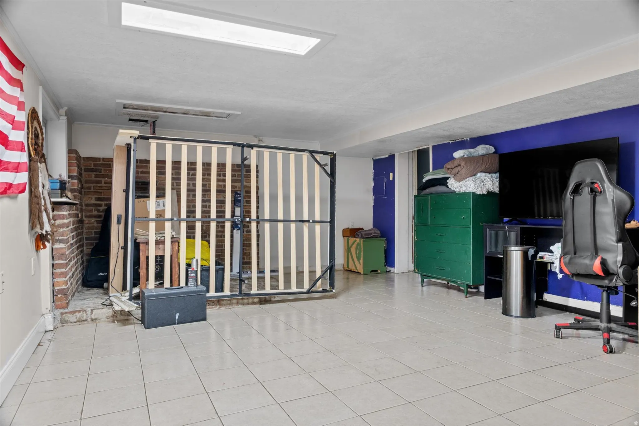 Spacious room featuring light-toned tile flooring, a brick-textured wall section, and a ceiling-mounted rectangular light fixture