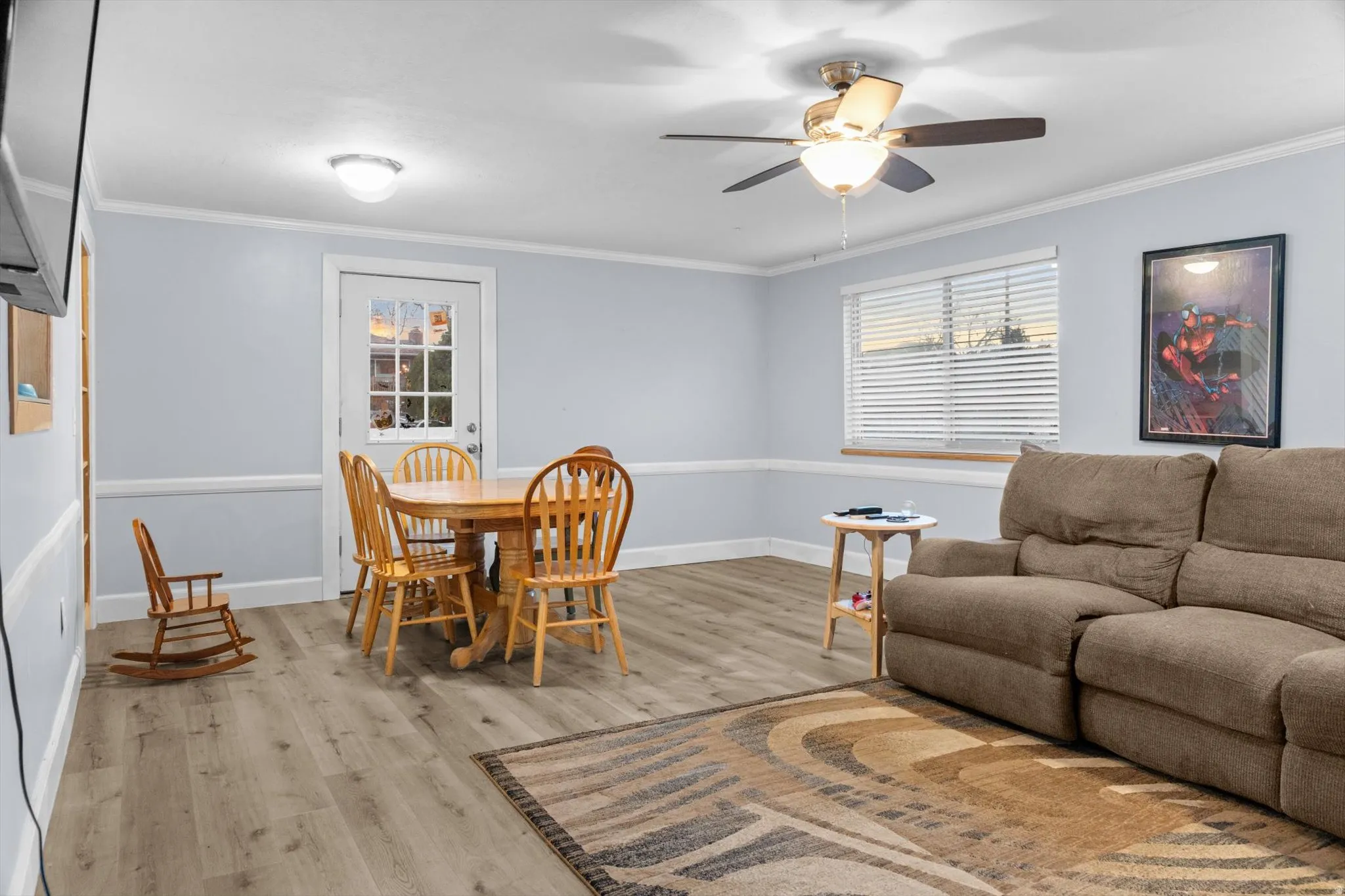 Spacious room featuring wood-finish flooring, a ceiling fan with integrated lighting, and multiple windows with horizontal blinds