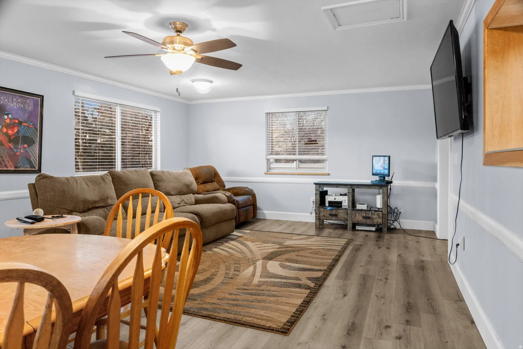 Spacious living area featuring light wood-finish flooring, two large windows with blinds, and light blue walls with white trim