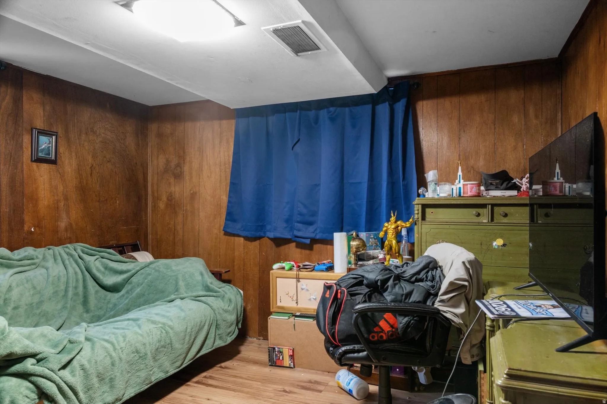 Room featuring wood-paneled walls, a single window with blue curtains, and wood-finish flooring