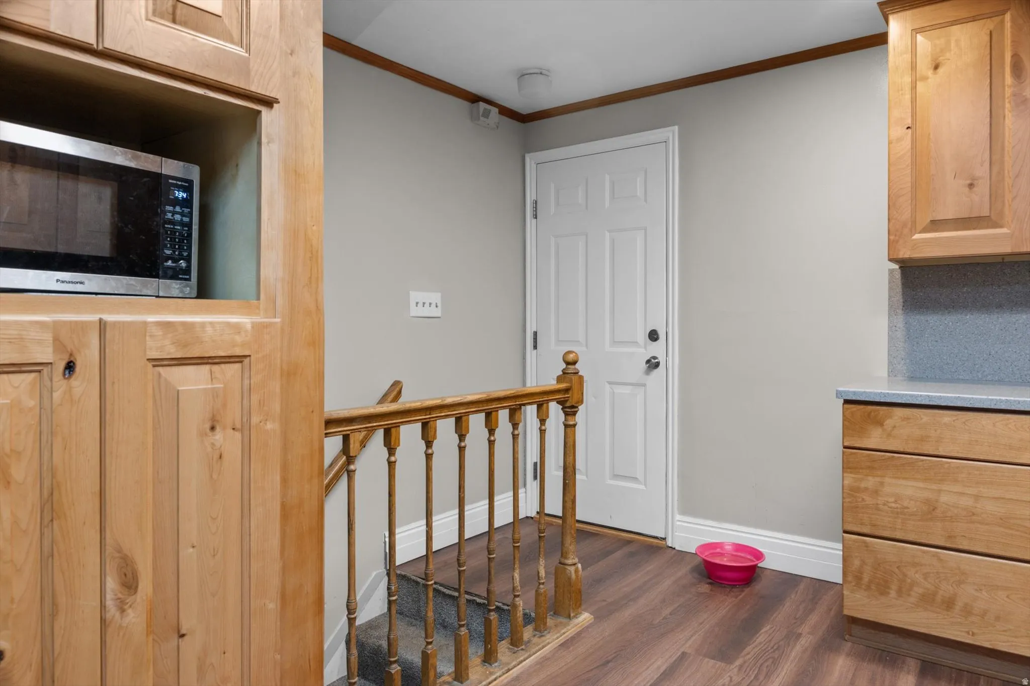 Built-in cabinetry with a dedicated microwave niche, wood-finish flooring, light gray walls, and a wood banister