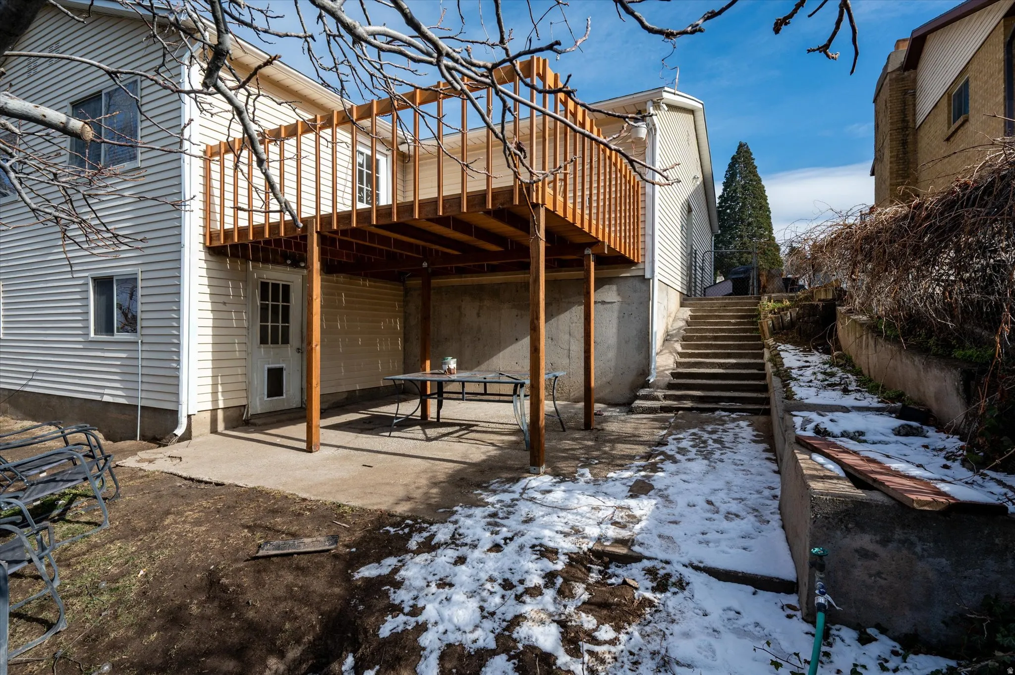 Rear elevation of a residence featuring light-colored siding, a second-story wooden deck, and a ground-level concrete patio