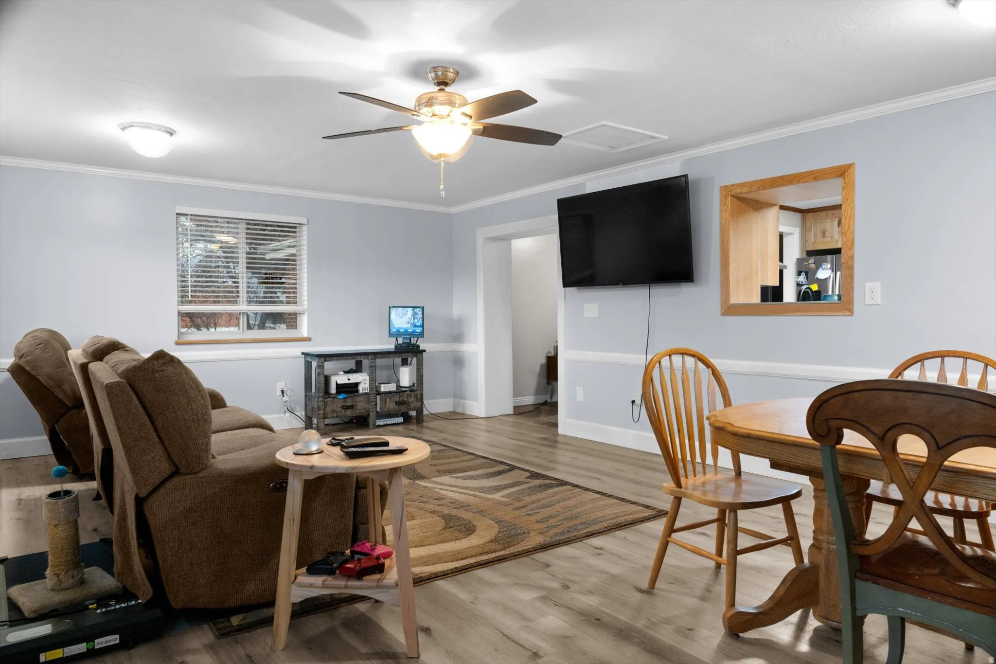 Spacious living area featuring wood-finish flooring, light gray walls with white wainscoting, and white crown molding