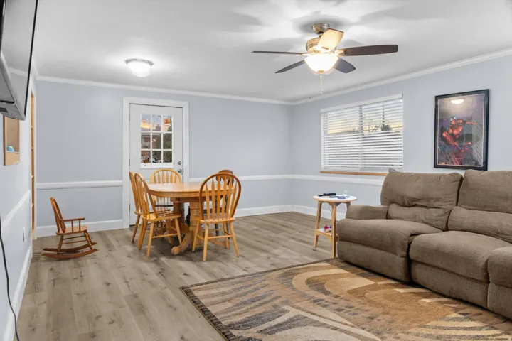 Spacious room featuring wood-finish flooring, a ceiling fan with integrated lighting, and multiple windows with horizontal blinds