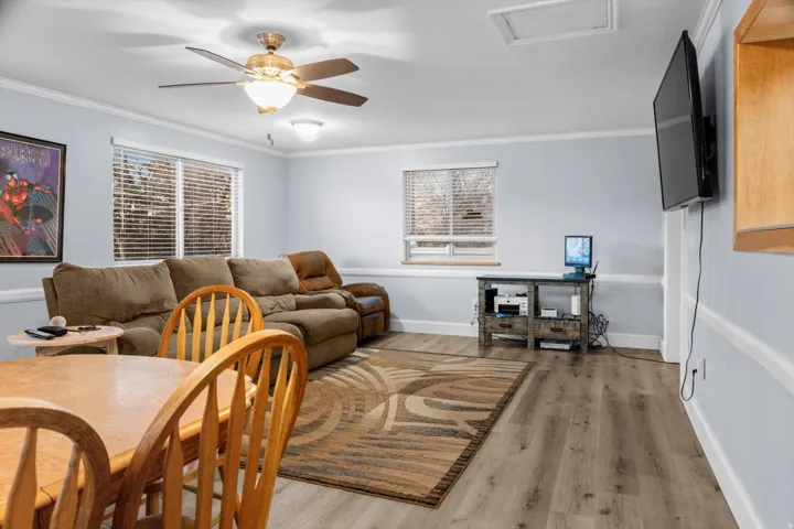 Spacious living area featuring light wood-finish flooring, two large windows with blinds, and light blue walls with white trim