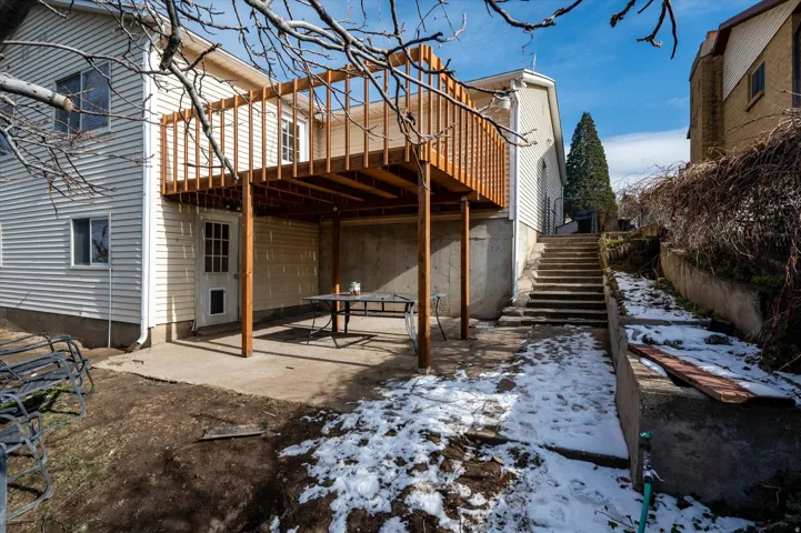 Rear elevation of a residence featuring light-colored siding, a second-story wooden deck, and a ground-level concrete patio