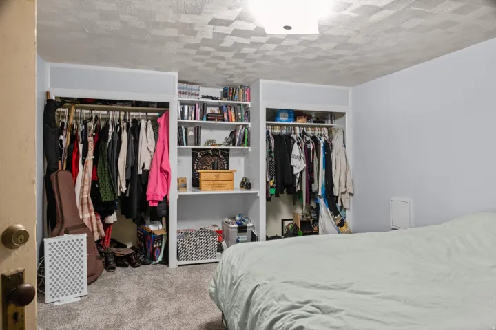 Bedroom featuring built-in shelving, two open closet spaces, and carpet flooring