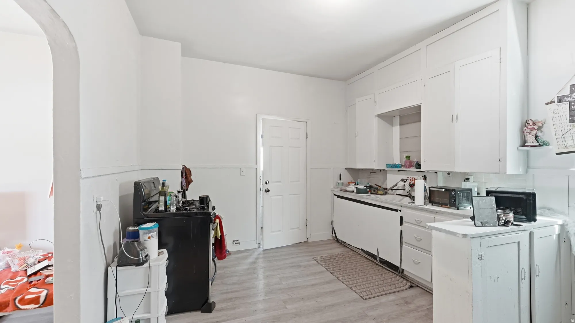 White cabinetry offering abundant storage, wood-finish flooring, and an arched doorway