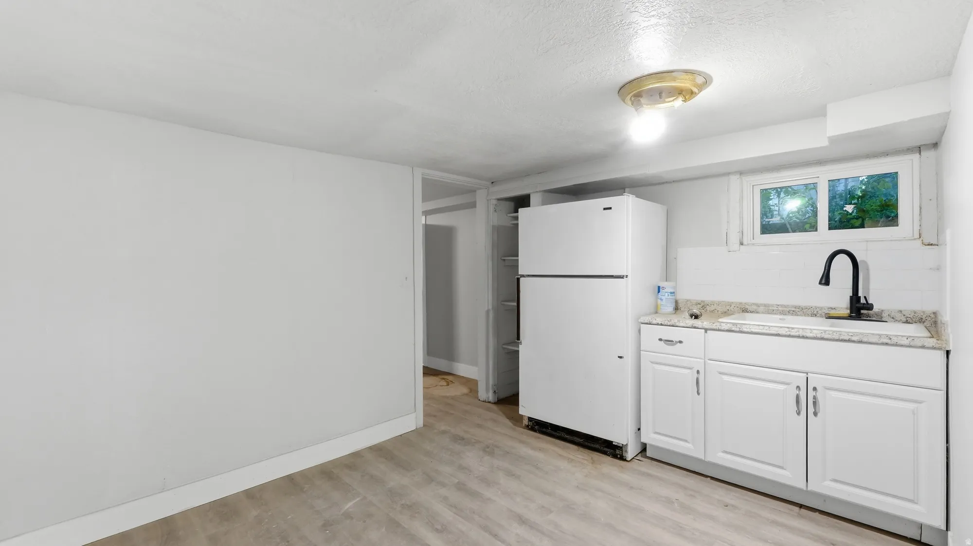 Kitchenette featuring white cabinetry, a black gooseneck faucet, an undermount sink, and light-toned countertops