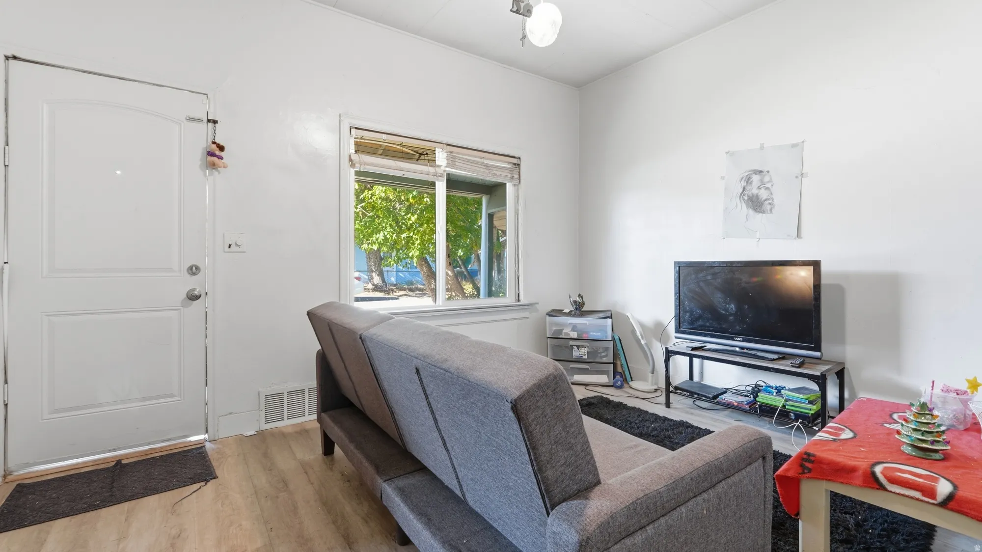 Light wood-finish flooring, white walls, and a white entry door with a decorative arch panel