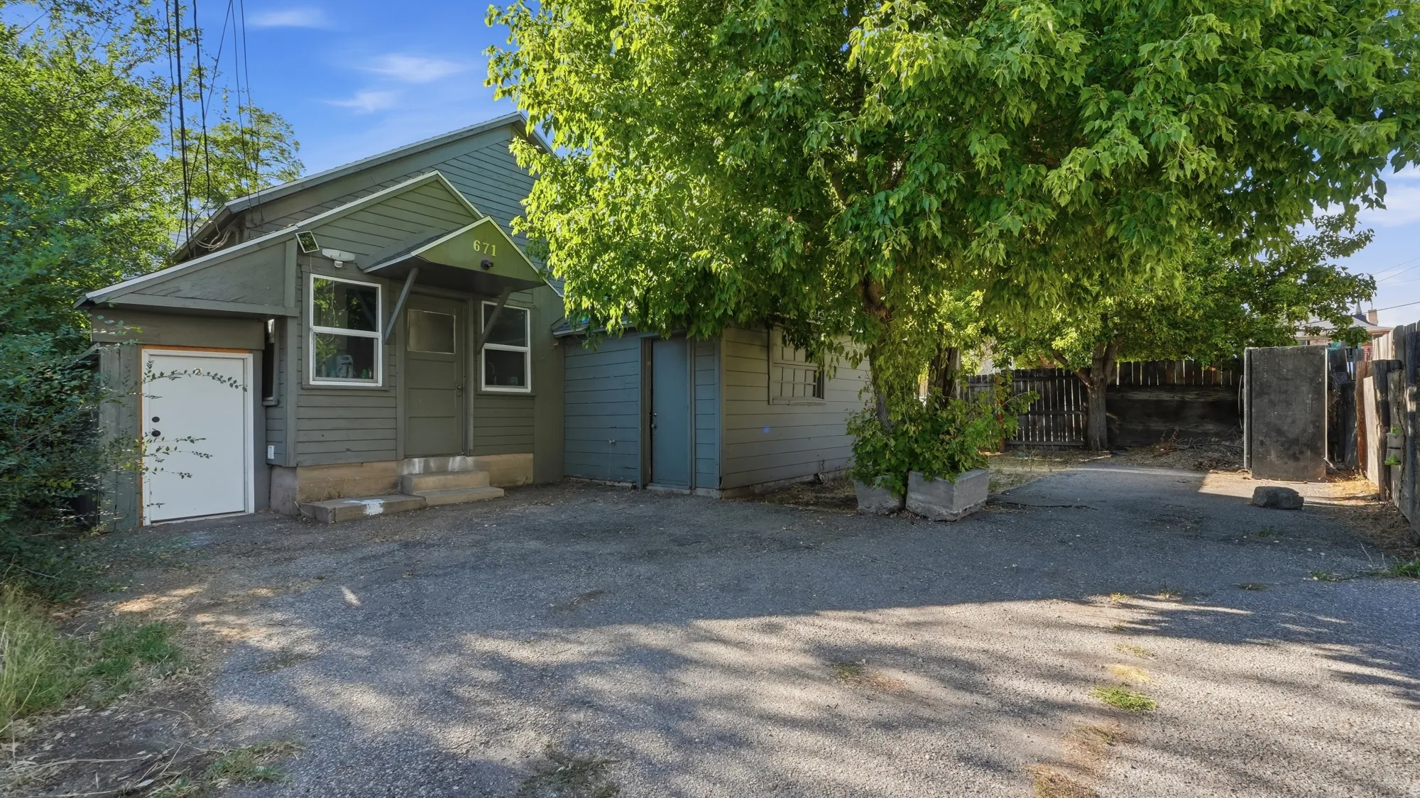 Gravel driveway leading to a residence with green siding, multiple windows, and a covered entry