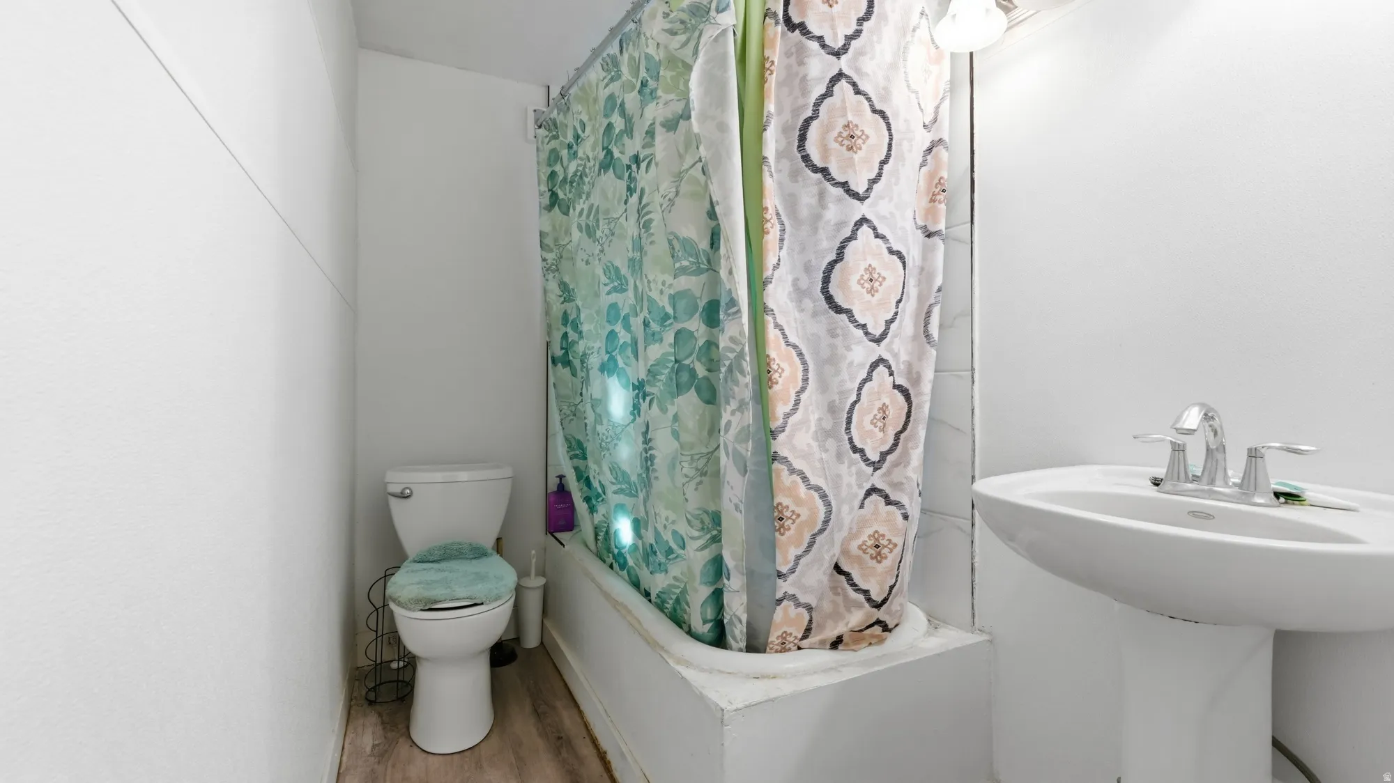 Pedestal sink with chrome fixtures, white toilet, and wood-finish flooring
