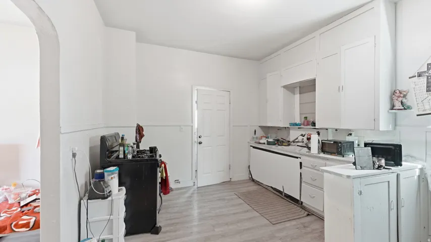 White cabinetry offering abundant storage, wood-finish flooring, and an arched doorway