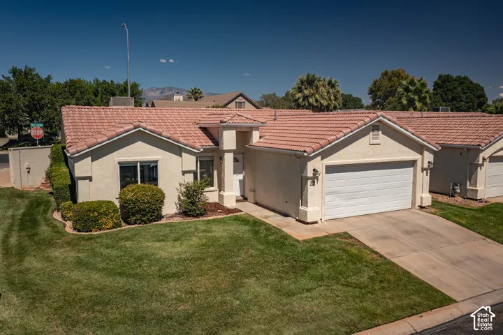 Stucco exterior with a terracotta tile roof, attached two-car garage, concrete driveway, and front landscaping