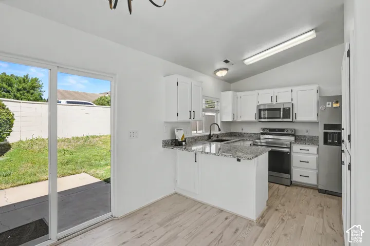 Kitchen featuring white cabinetry, stainless steel appliances, stone-finish countertops, wood-finish flooring, and vaulted ceiling