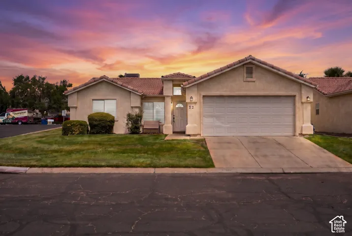 Stucco exterior with a tile roof, an attached two-car garage, concrete driveway, and front lawn with mature shrubs