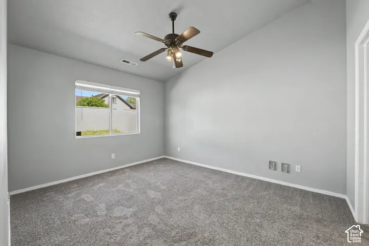 Spacious room featuring vaulted ceilings, a ceiling fan with integrated lighting, and a large window with blinds