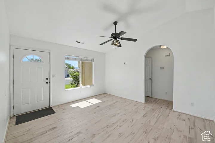 White paneled entry door with an arched window, wood-finish flooring, vaulted ceiling, and an arched doorway