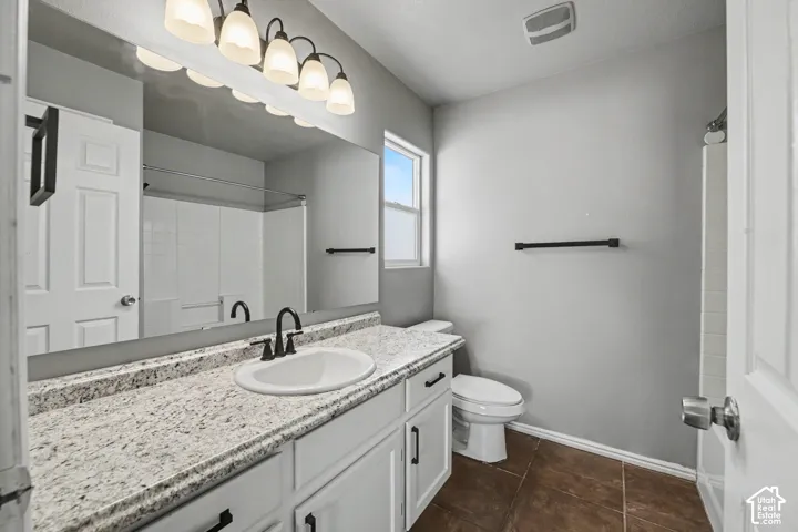 Bathroom featuring a white vanity with a speckled countertop, a rectangular mirror, a window, and a shower with white subway tile