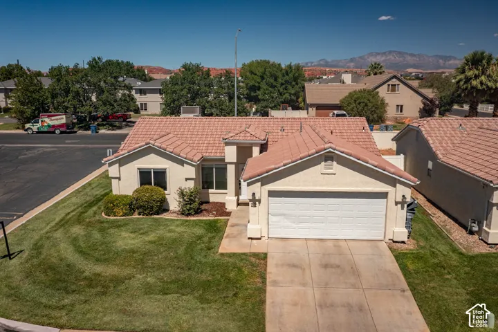 Stucco exterior with a tiled roof, attached two-car garage, concrete driveway, and established front landscaping
