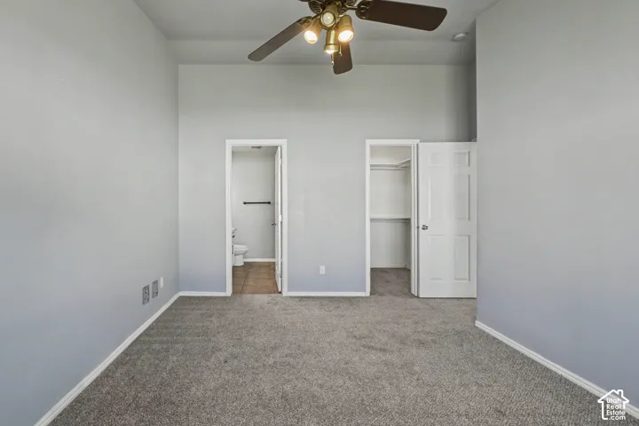 Neutral-toned carpeting and walls, overhead ceiling fan with lighting, two panel doors, and a tiled floor in the adjoining space