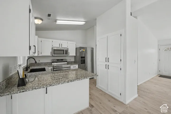 Kitchen featuring white cabinetry, granite-style countertops, a stainless steel sink with a matte black faucet, and wood-finish flooring