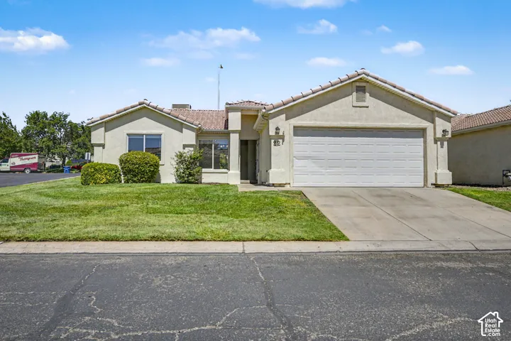 Stucco exterior with a tiled roof, attached two-car garage, concrete driveway, and a manicured front lawn