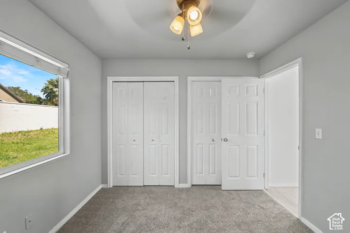 Room with light gray walls, gray carpet, a ceiling fan with light fixture, and a window with blinds