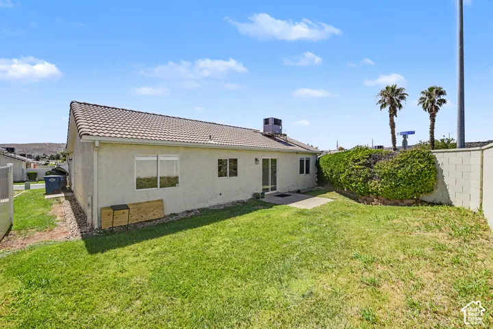 Expansive grassy yard with a concrete patio, stucco exterior, and a tiled roof