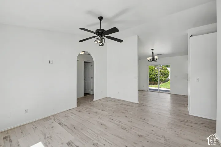 Wood-finish flooring throughout, arched doorway, black ceiling fan with integrated lighting, sliding glass door, and backyard landscaping