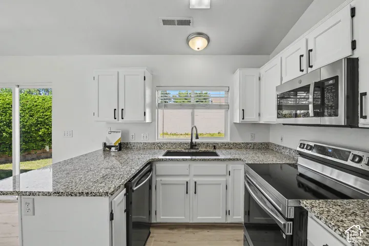 U-shaped kitchen with stone-finish countertops, white cabinetry, and stainless steel appliances