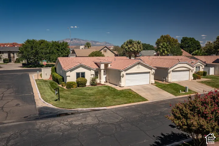 Stucco exterior with a tile roof, an attached two-car garage, and a manicured lawn