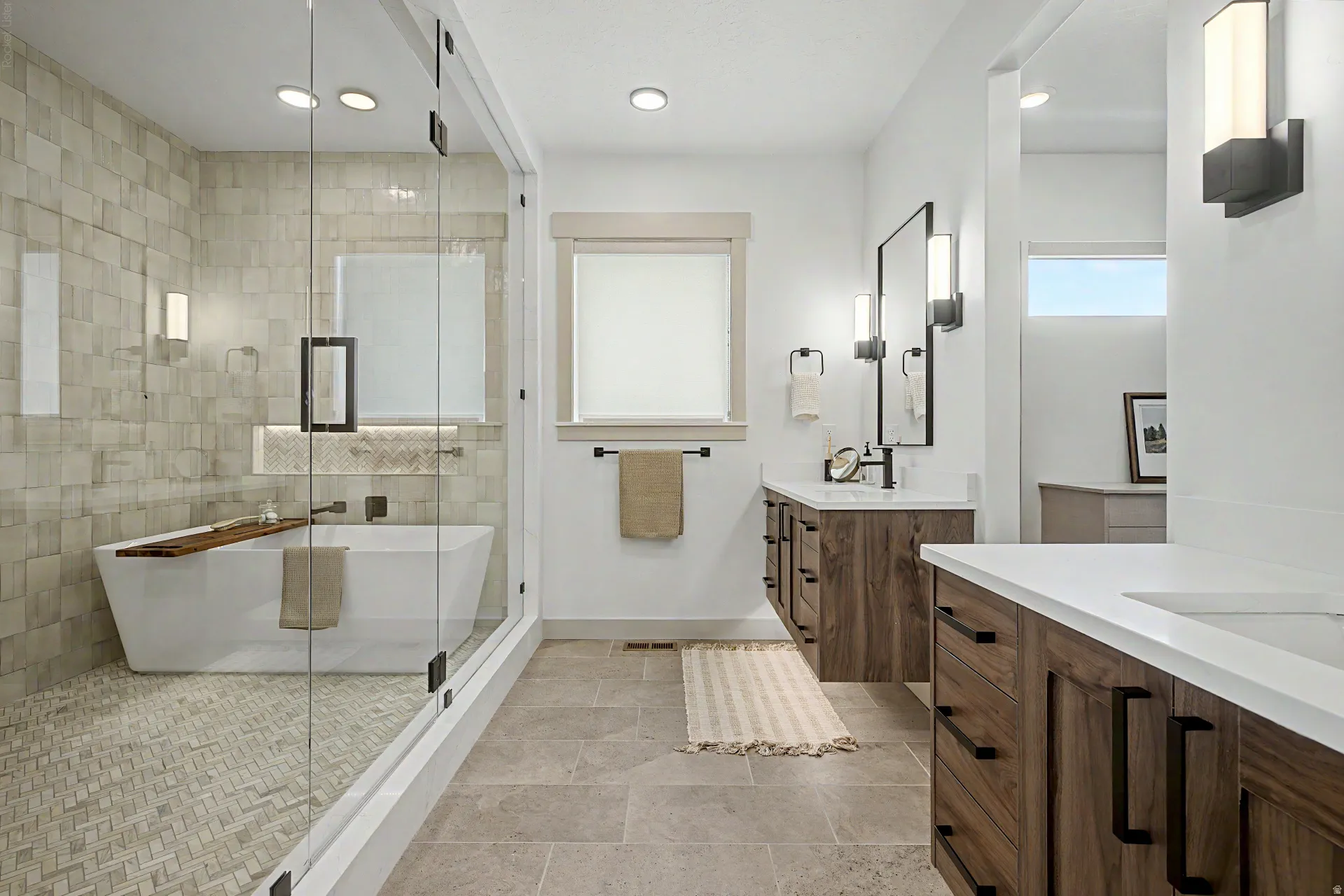 Walk-in shower with glass enclosure, freestanding soaking tub, dual floating wood-finish vanities, quartz countertops, and contemporary lighting fixtures