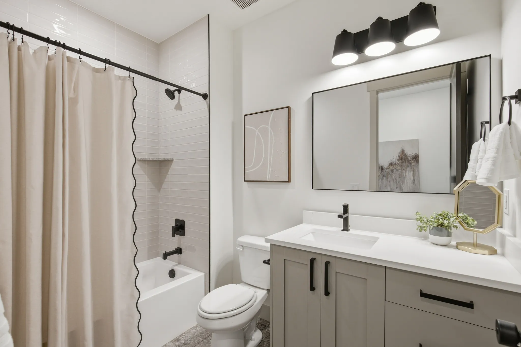 Bathroom featuring a white bathtub, tiled shower surround with built-in shelf, gray vanity with white countertop, and black framed mirror