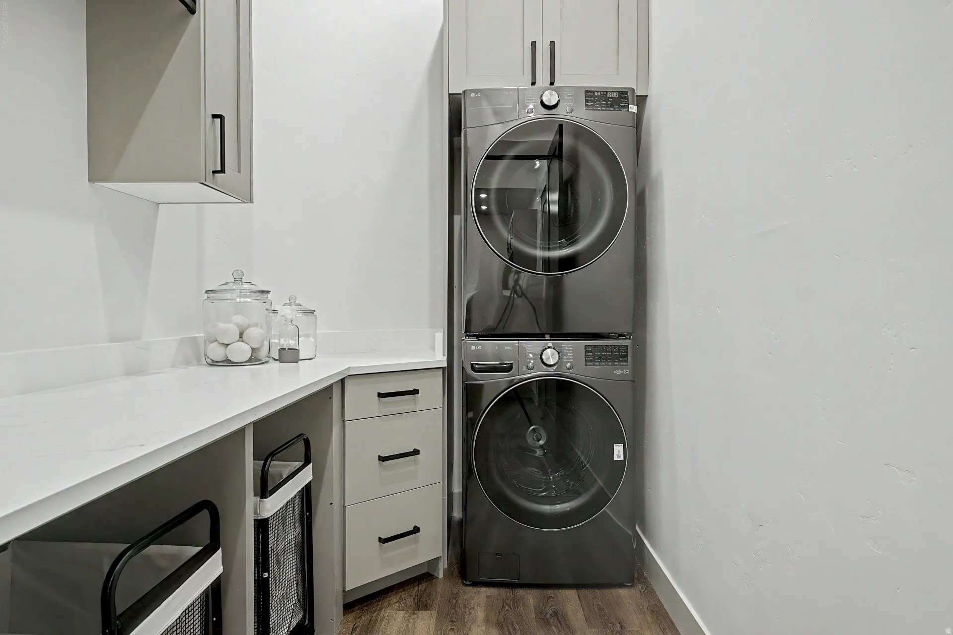 Dedicated laundry area featuring a stacked washer and dryer, light gray cabinetry with black hardware, and a white countertop