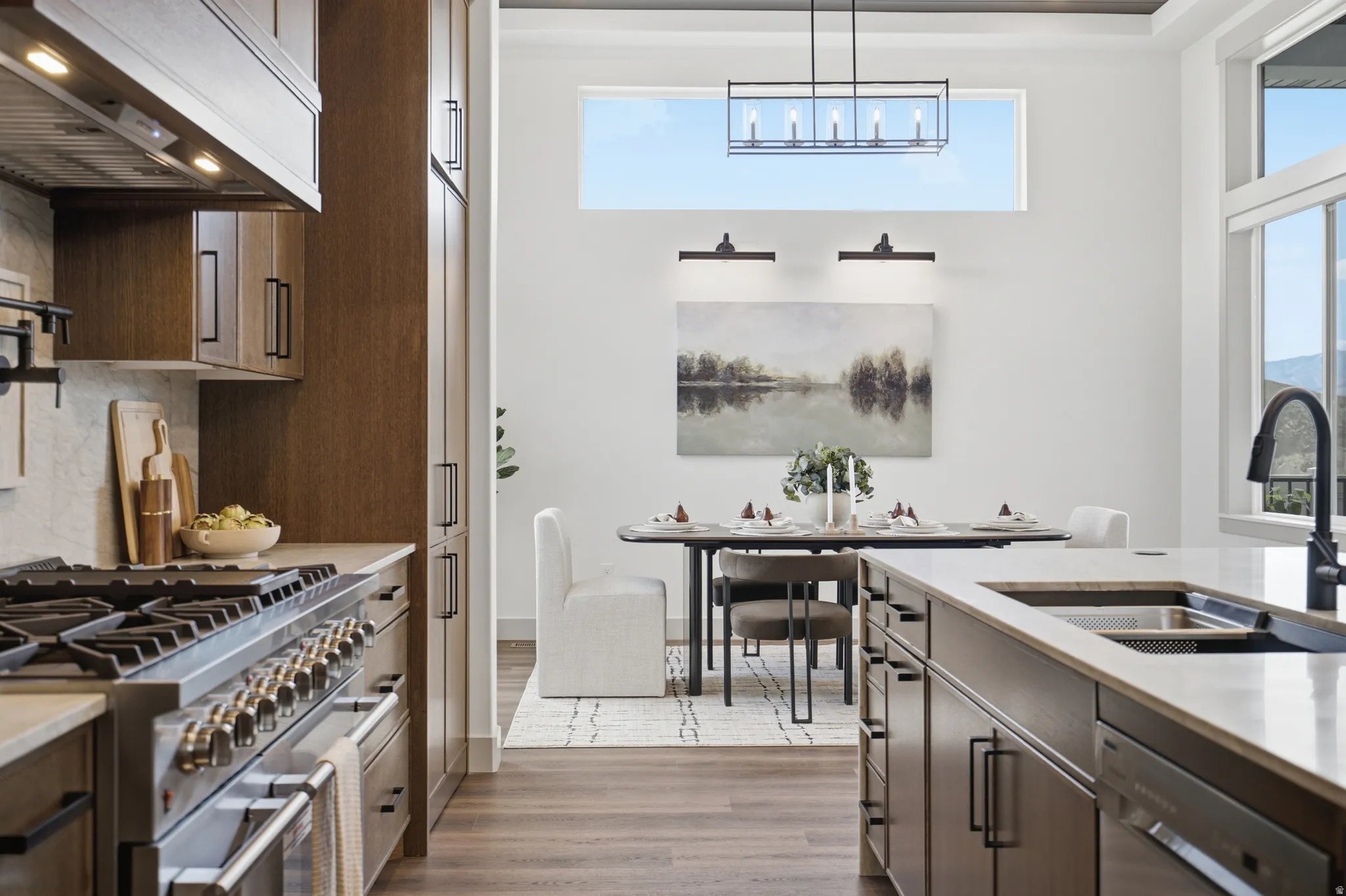 Gourmet kitchen featuring a stainless steel gas range, built-in cabinetry with black hardware, and a center island with an undermount sink and gooseneck faucet