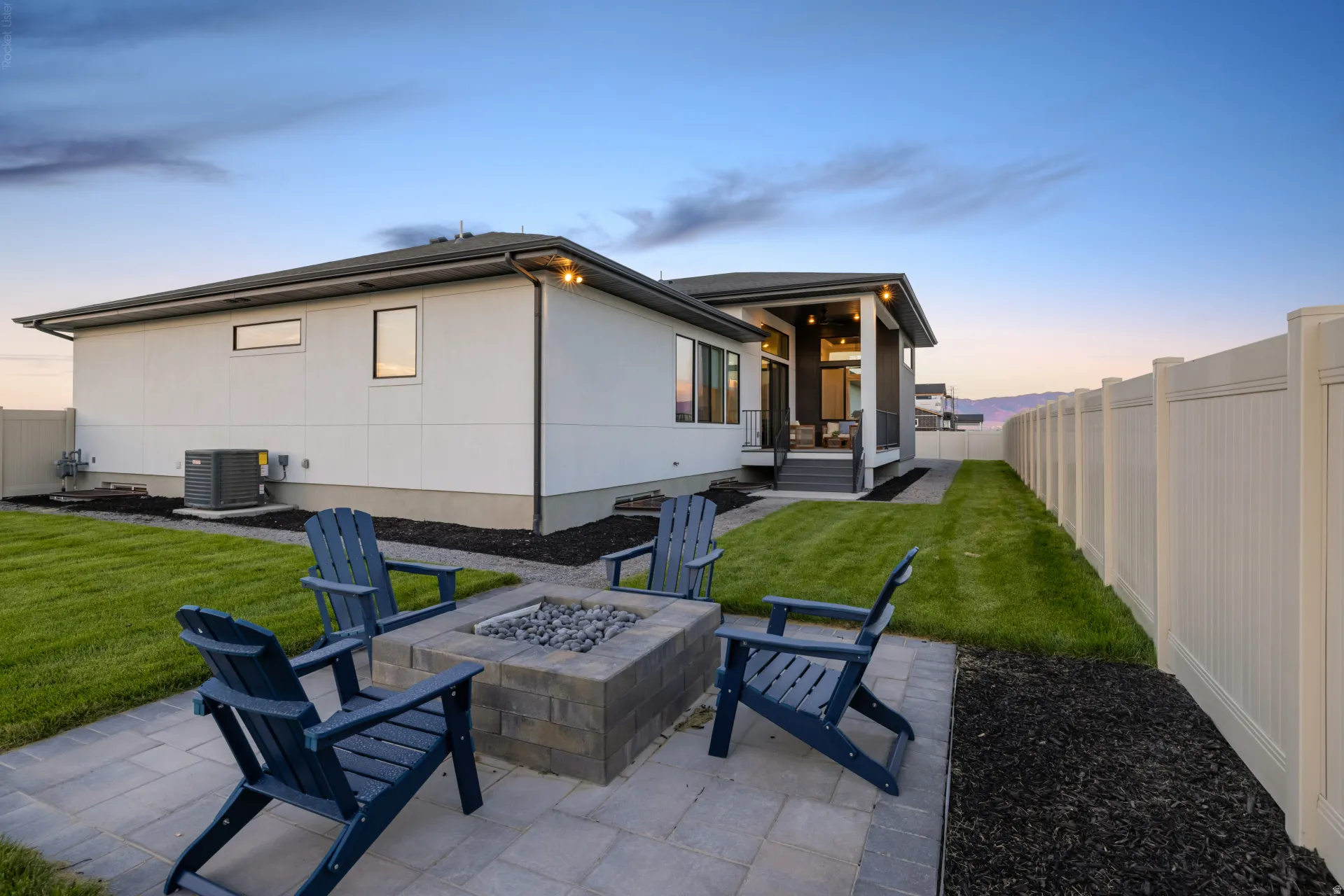 Expansive backyard featuring a paver patio with a built-in fire pit, manicured lawn, and privacy fencing