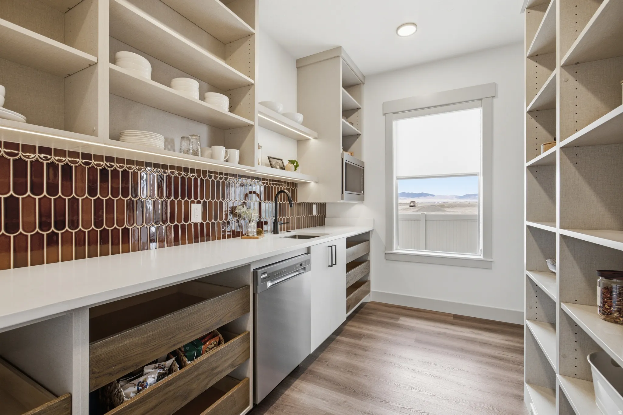 Modern pantry featuring extensive open shelving, rich brown tile backsplash, white countertops, built-in stainless steel dishwasher, and wood-finish flooring